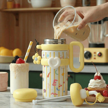 A person pouring an iced drink into a colourful yellow thermos flask with cartoon designs on a kitchen counter.