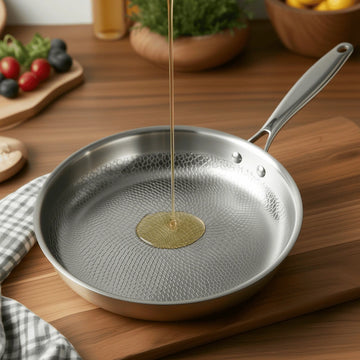 German Stainless Steel Hammered Non-Stick Pattern frying pan on a wooden table with oil being poured into it