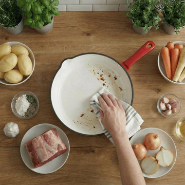 A top view of a Red enameled cast iron pan with premium non-toxic enamel coating, induction compatible, high-heat cooking ready, and easy-to-clean surface. Perfect for everyday cooking, durable and long-lasting. being wiped clean with a cloth.
