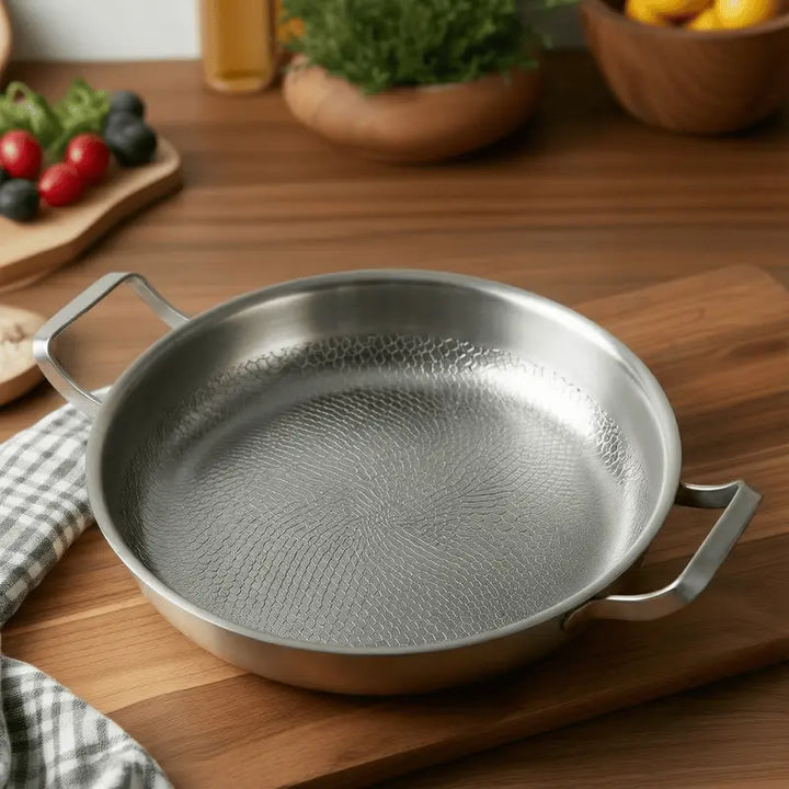 Titanium Hammered Double-Handle Frying Pan on a wooden surface with vegetables in the background