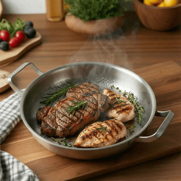 Steaks with herbs in a Titanium Hammered Double-Handle Frying Pan on a wooden table with vegetables in the background