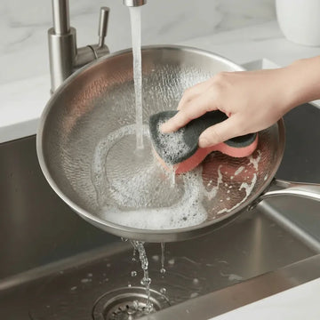 Non-toxic titanium hammered wok with 3-ply construction, induction-ready stainless steel base and ergonomic stay-cool handle being washed up in the sink with soapy water and a sponge.